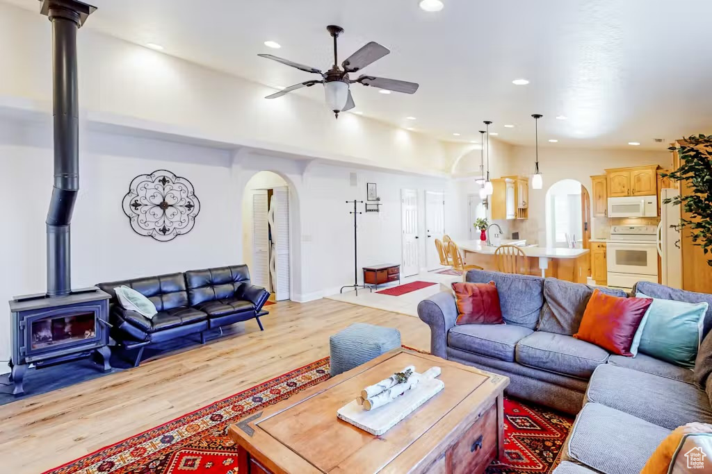 Living room featuring arched walkways, a wood stove, ceiling fan, light wood-type flooring, and recessed lighting