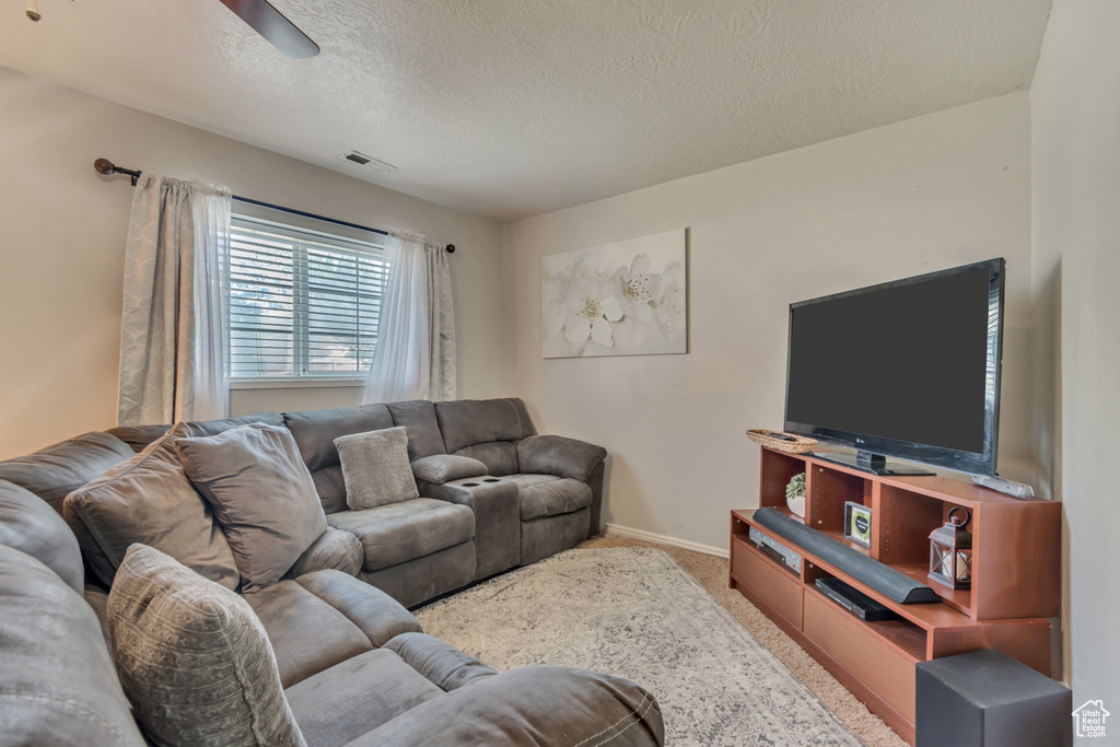 Living room with a textured ceiling, carpet, baseboards, and ceiling fan