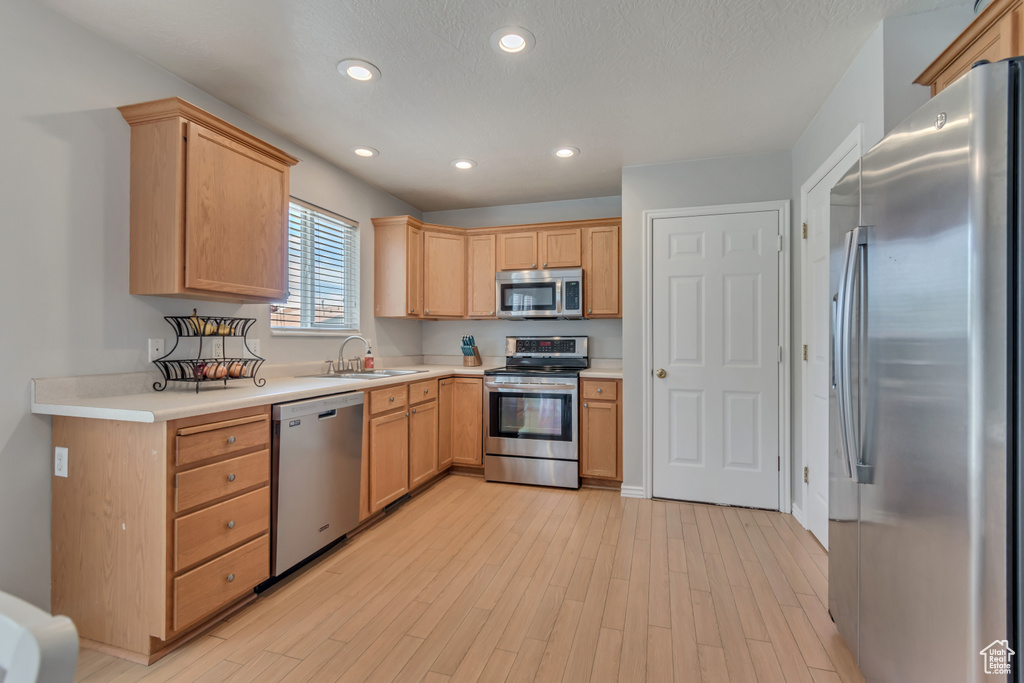 Kitchen with stainless steel appliances, a sink, light wood finished floors, light countertops, and recessed lighting