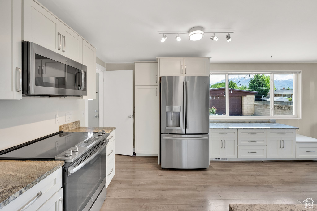 Kitchen featuring stainless steel appliances, light wood-style floors, light stone countertops, and white cabinetry