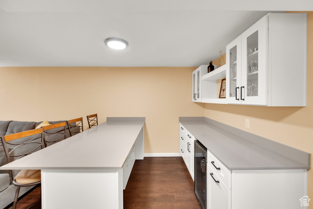 Kitchen featuring a peninsula, wine cooler, a kitchen bar, glass insert cabinets, and dark wood finished floors