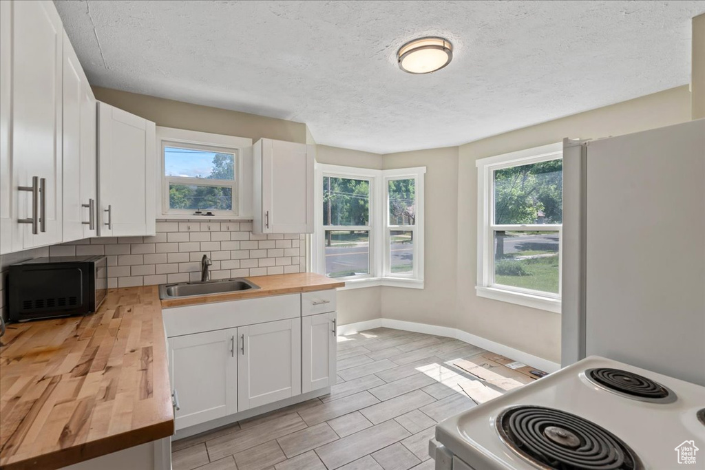 Kitchen featuring wooden counters, a sink, black microwave, baseboards, and stove