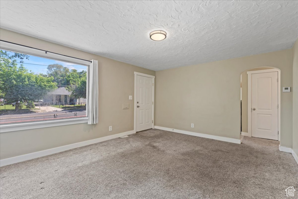 Unfurnished room featuring arched walkways, a textured ceiling, carpet flooring, and baseboards