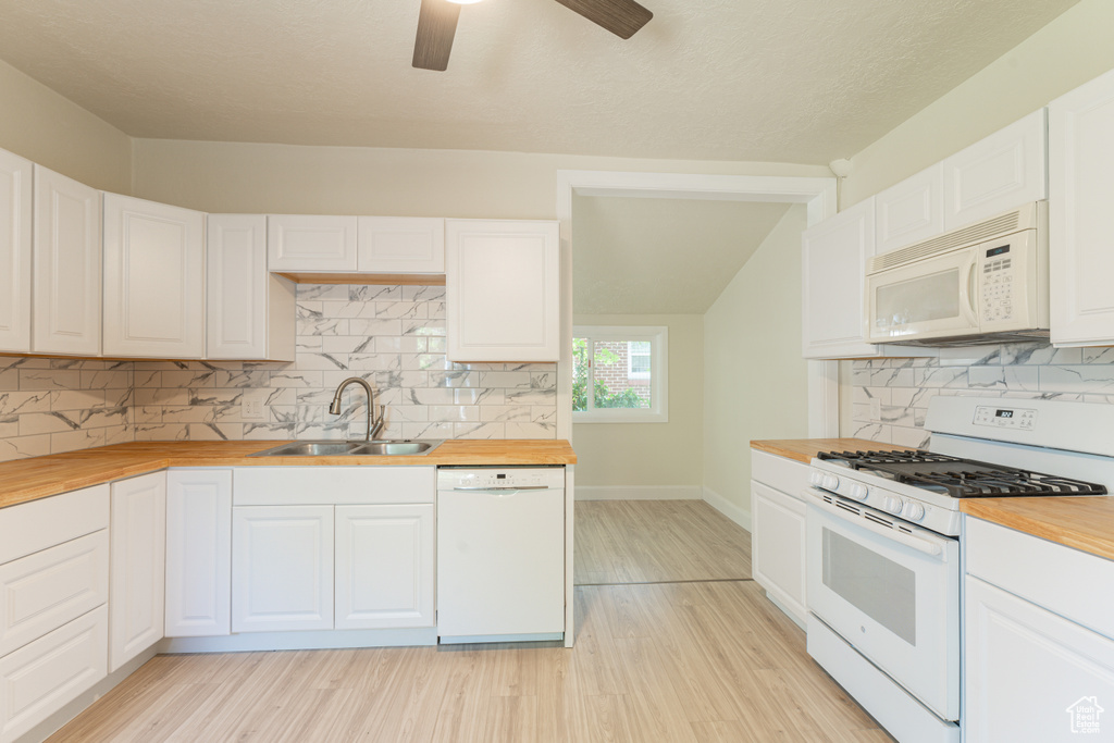 Kitchen featuring white appliances, butcher block countertops, a sink, light wood finished floors, and vaulted ceiling