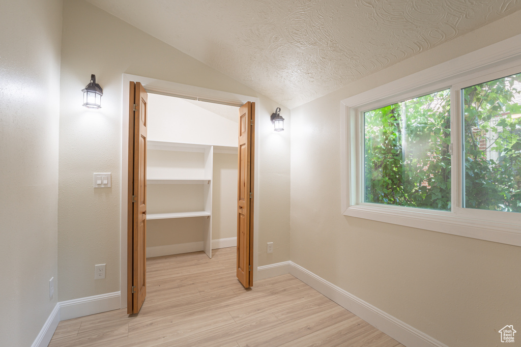 Hall with lofted ceiling, light wood-style flooring, a textured ceiling, and baseboards