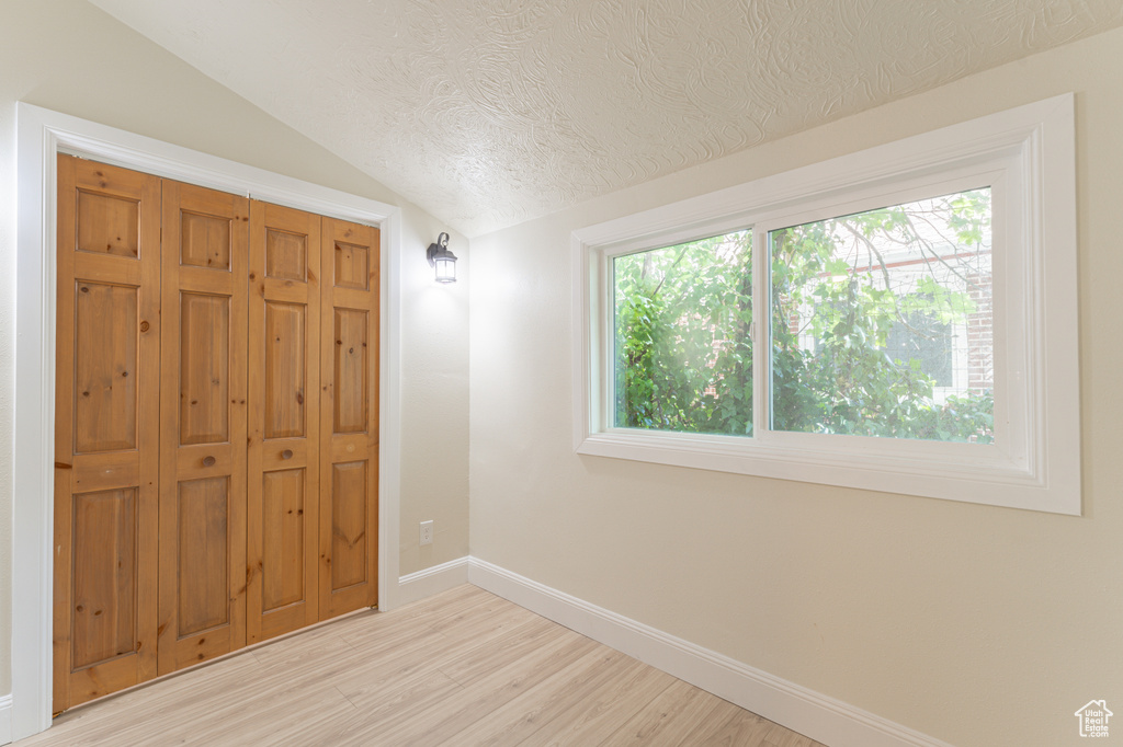 Unfurnished bedroom with a textured ceiling, lofted ceiling, light wood-style floors, baseboards, and a closet