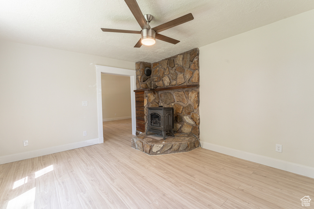 Unfurnished living room featuring a wood stove, ceiling fan, wood finished floors, a textured ceiling, and baseboards