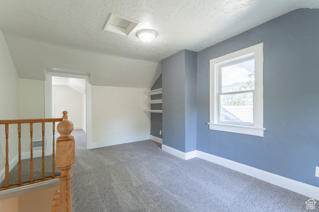 Bonus room with carpet, lofted ceiling, a textured ceiling, attic access, and baseboards