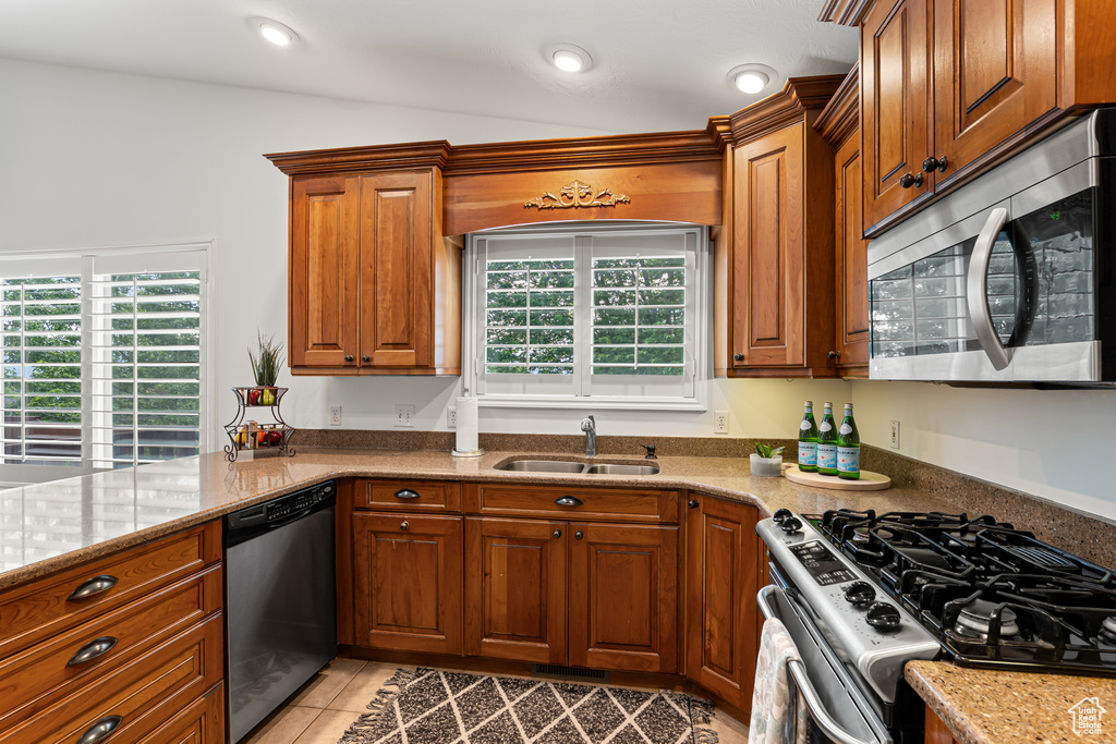Kitchen featuring stainless steel appliances, a sink, brown cabinetry, light stone counters, and recessed lighting