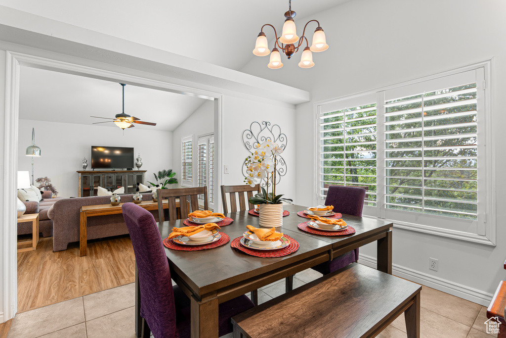 Dining space featuring vaulted ceiling, light tile patterned floors, a ceiling fan, and a chandelier