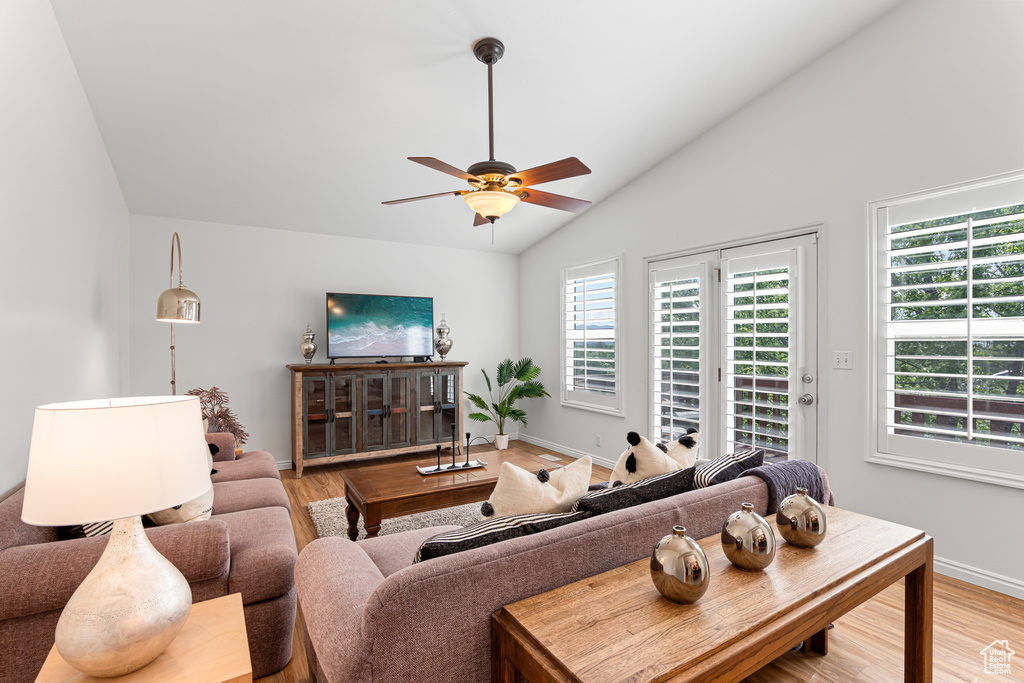 Living room featuring lofted ceiling, light wood-style floors, a ceiling fan, and baseboards