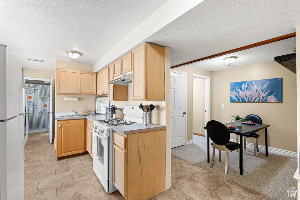 Kitchen featuring white appliances, light brown cabinetry, a textured ceiling, under cabinet range hood, and baseboards