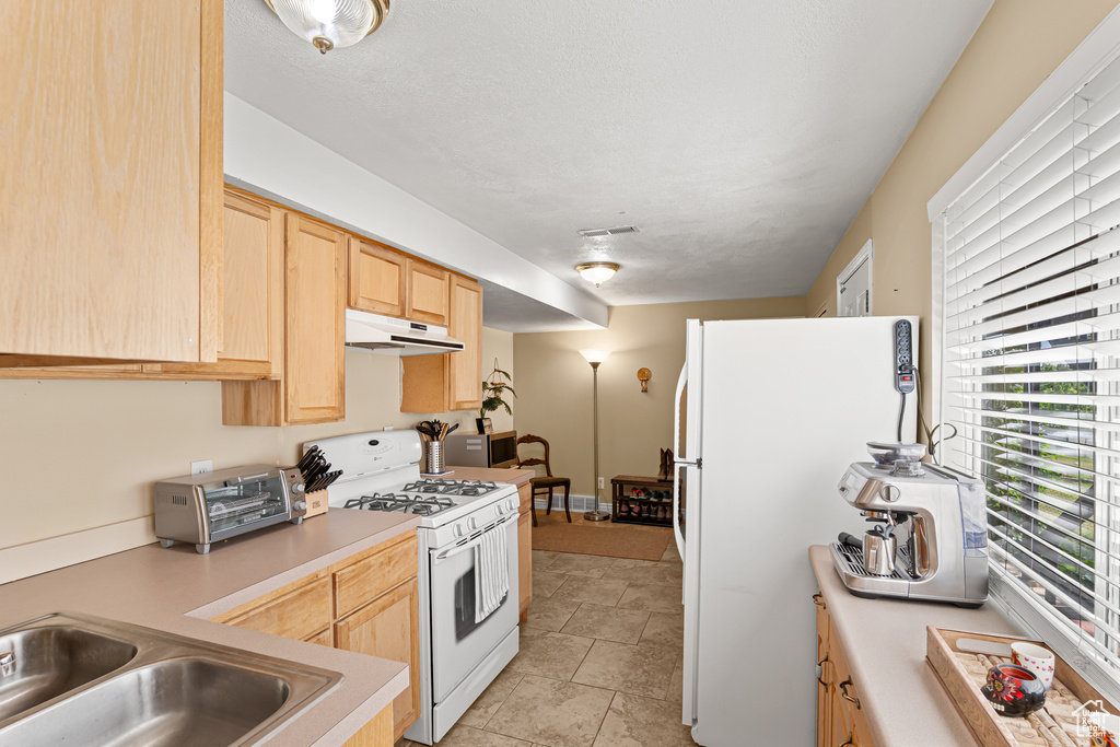 Kitchen featuring white appliances, under cabinet range hood, light brown cabinetry, and light countertops
