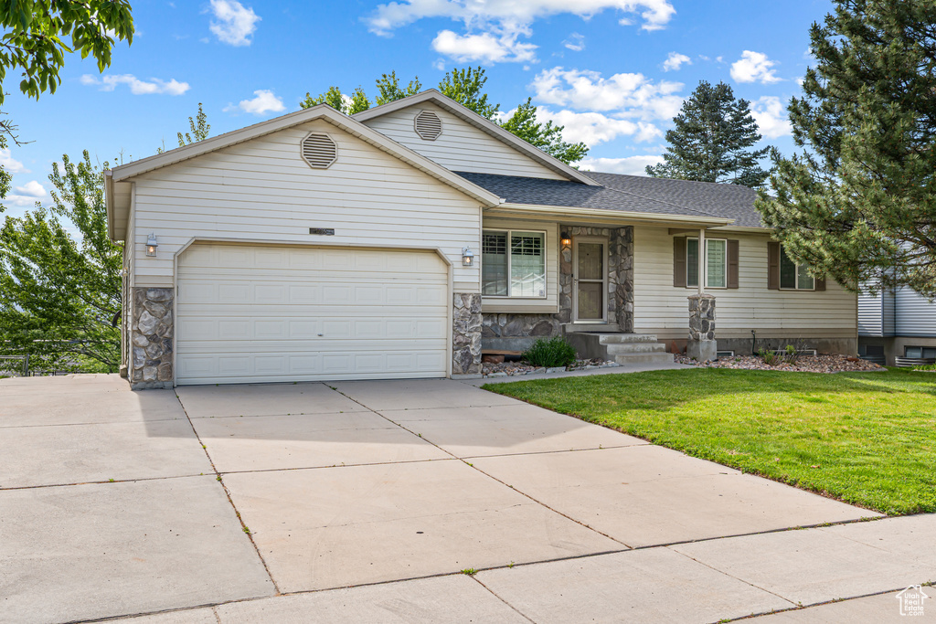 View of front facade featuring stone siding, concrete driveway, a garage, and a front yard