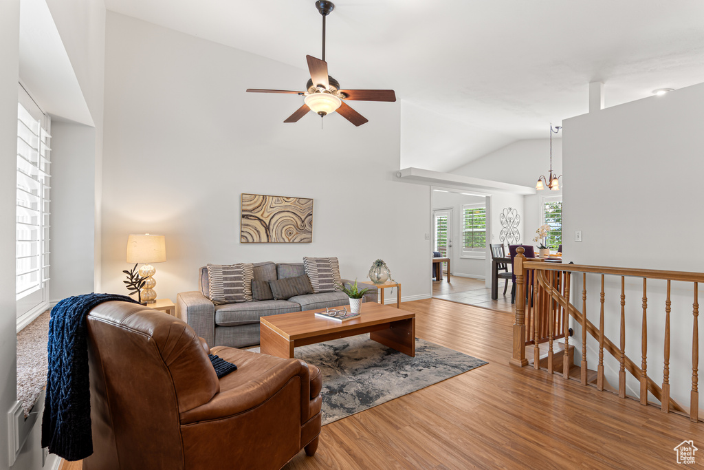 Living area with a ceiling fan, vaulted ceiling, wood finished floors, a chandelier, and baseboards