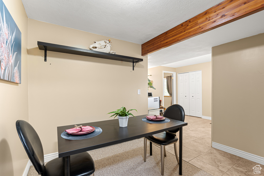 Dining area featuring baseboards, light tile patterned floors, beam ceiling, and a textured ceiling