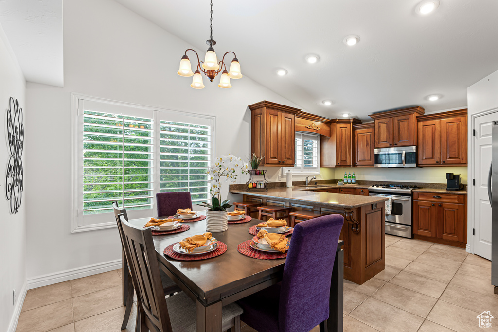 Kitchen featuring stainless steel appliances, vaulted ceiling, a chandelier, a sink, and brown cabinetry