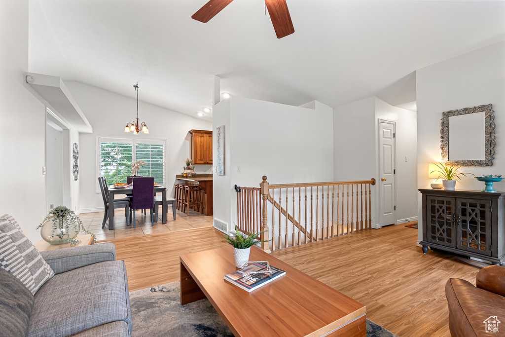 Living area featuring a ceiling fan, vaulted ceiling, light wood-style floors, a chandelier, and baseboards