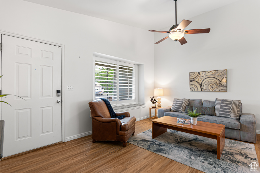 Living area with wood finished floors, ceiling fan, baseboards, and a towering ceiling