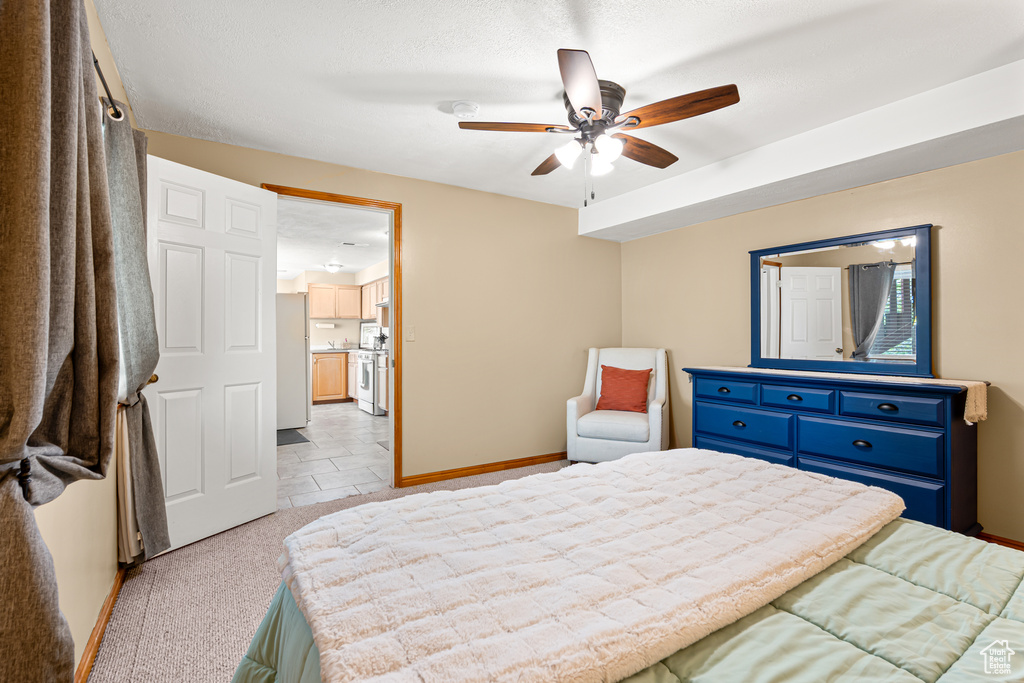 Bedroom featuring baseboards, freestanding refrigerator, ceiling fan, and light carpet