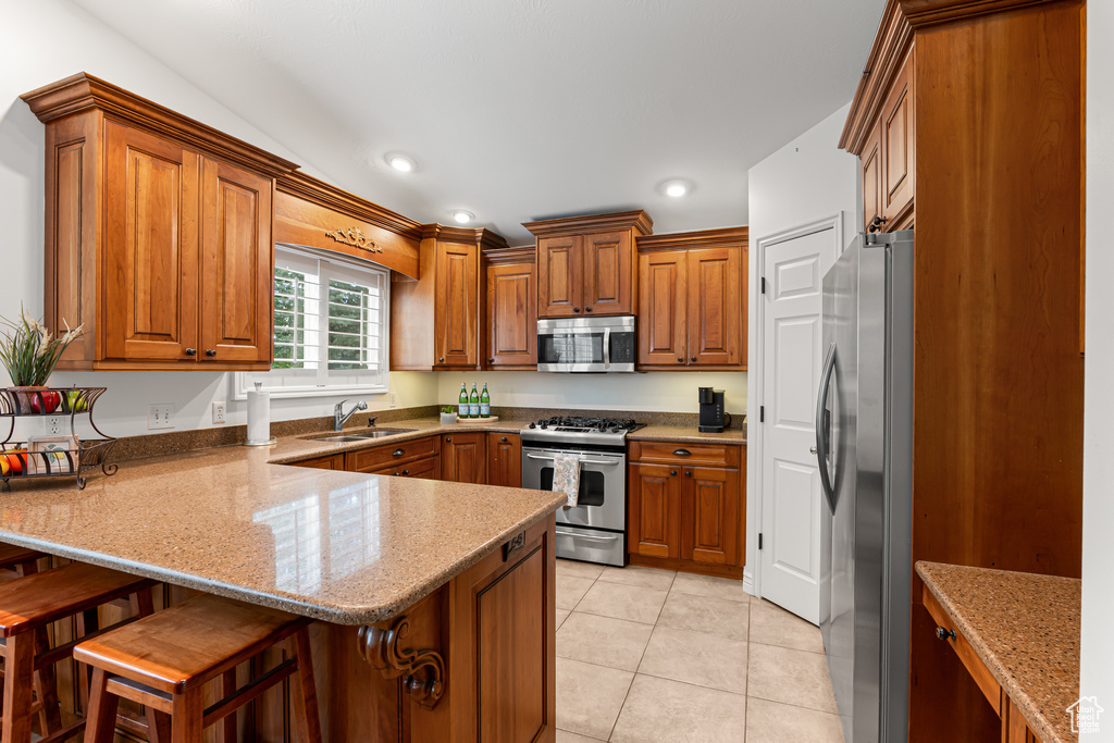 Kitchen featuring appliances with stainless steel finishes, a peninsula, a sink, brown cabinetry, and recessed lighting