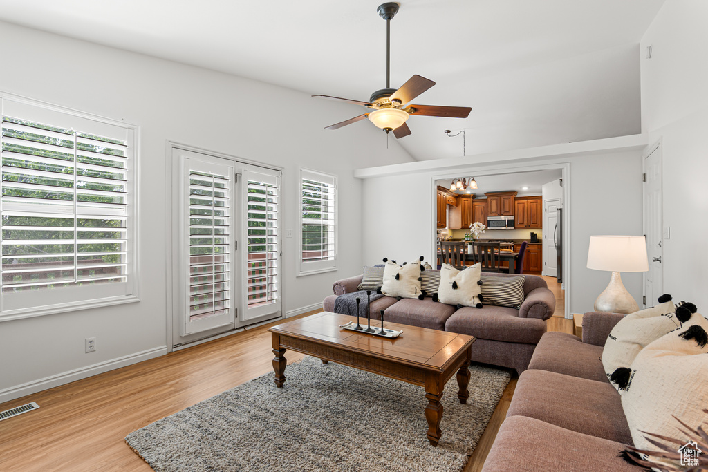 Living area with ceiling fan, light wood-style flooring, healthy amount of natural light, vaulted ceiling, and baseboards