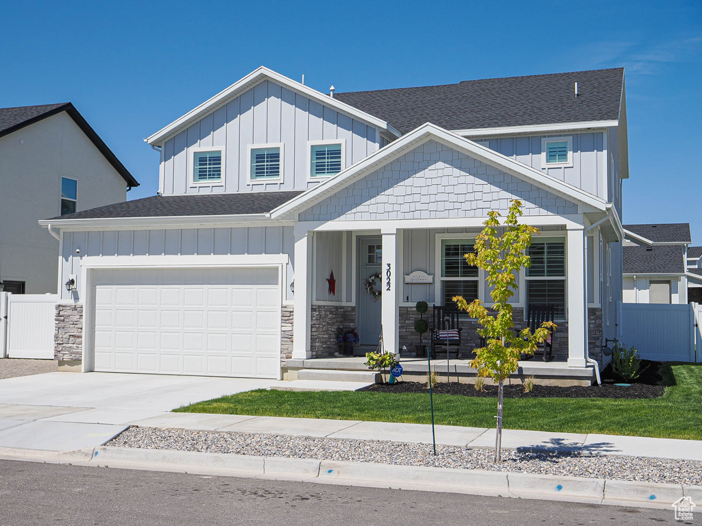 View of front of house featuring board and batten siding, a shingled roof, covered porch, driveway, and stone siding