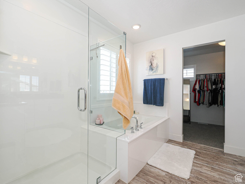 Bathroom with a shower stall, a bath, a spacious closet, wood finished floors, and baseboards