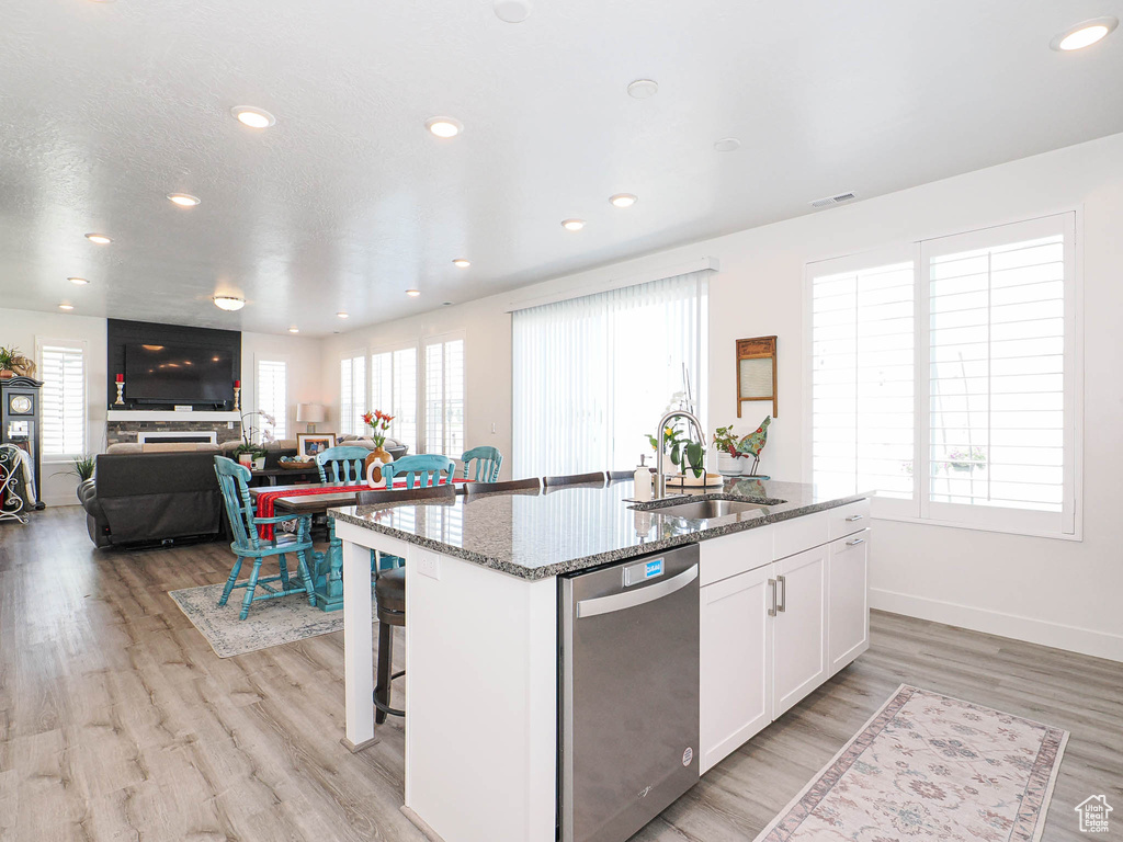 Kitchen featuring dishwasher, a sink, an island with sink, white cabinets, and dark stone countertops