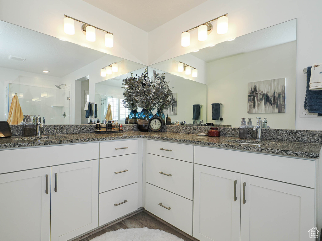 Bathroom featuring a shower stall, double vanity, and wood finished floors