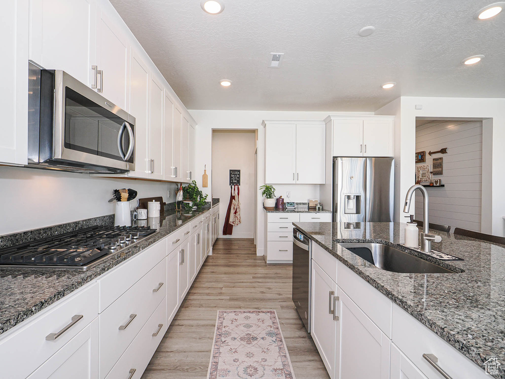 Kitchen featuring appliances with stainless steel finishes, a sink, light wood-style flooring, white cabinetry, and dark stone countertops