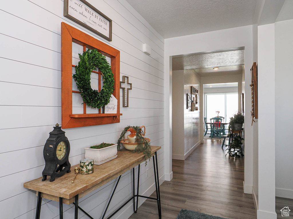 Hallway featuring wood finished floors, wood walls, baseboards, and a textured ceiling