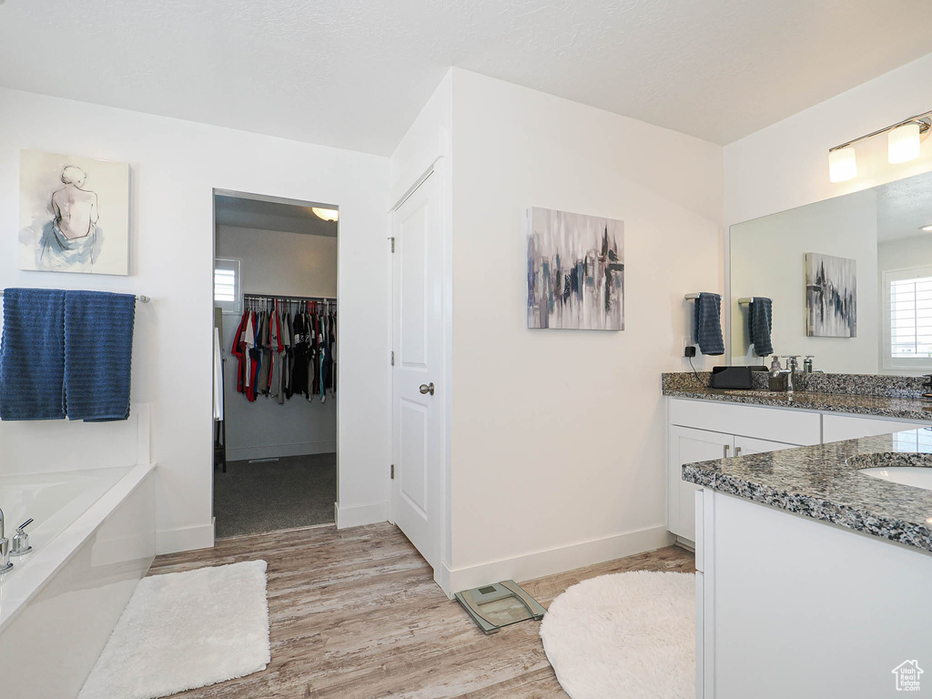 Full bath featuring wood finished floors, vanity, a bath, and baseboards