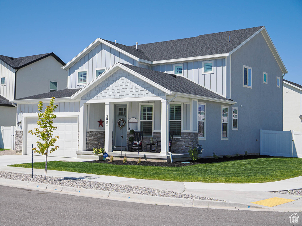 View of front of home with covered porch, board and batten siding, a garage, driveway, and roof with shingles