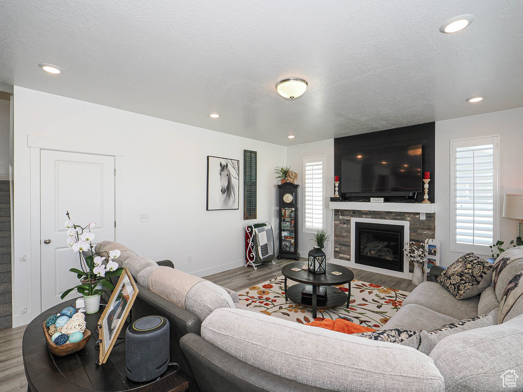 Living room with wood finished floors, a stone fireplace, baseboards, and recessed lighting