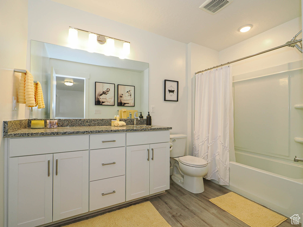 Full bath featuring double vanity, wood finished floors, toilet, and shower / bath combo