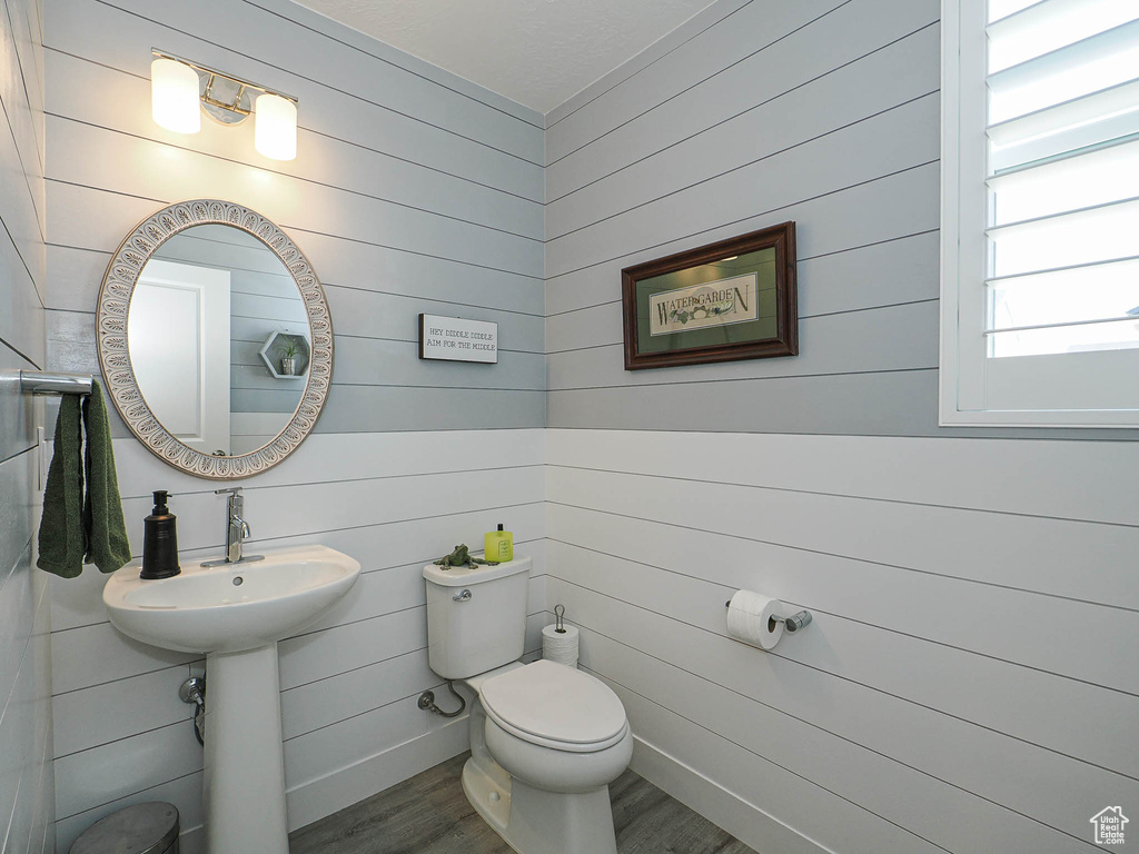Half bathroom featuring wood finished floors, toilet, and wooden walls