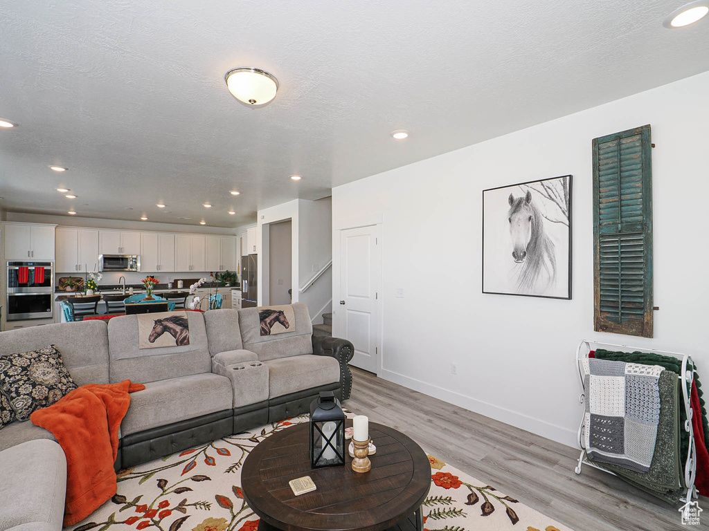 Living room with light wood-type flooring, recessed lighting, stairway, and baseboards