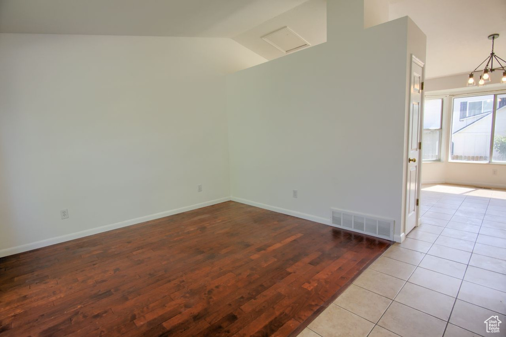 Spare room featuring wood finished floors, lofted ceiling, baseboards, and a chandelier