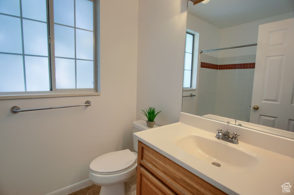 Bathroom featuring toilet, vanity, a shower, and baseboards