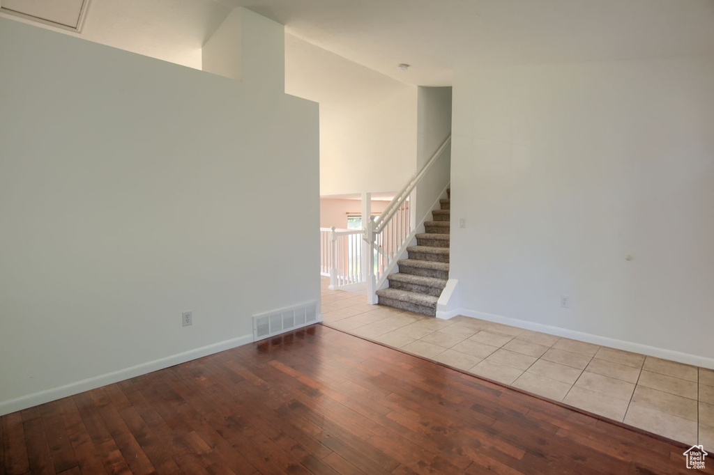 Unfurnished living room with hardwood / wood-style flooring, stairway, high vaulted ceiling, and baseboards