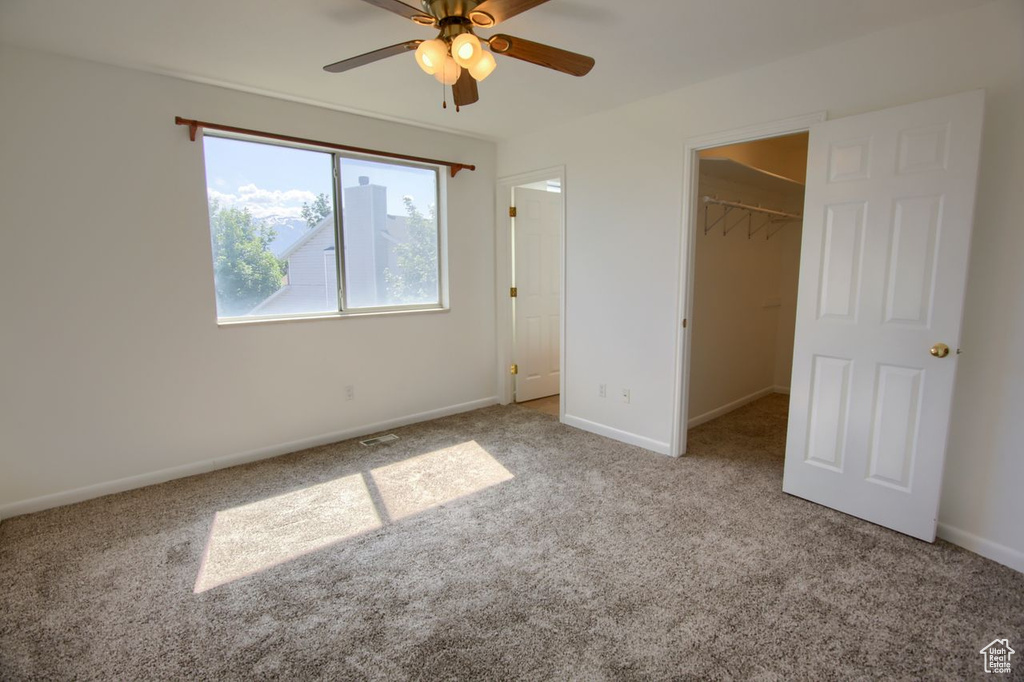 Unfurnished bedroom with carpet flooring, a spacious closet, baseboards, a closet, and ceiling fan