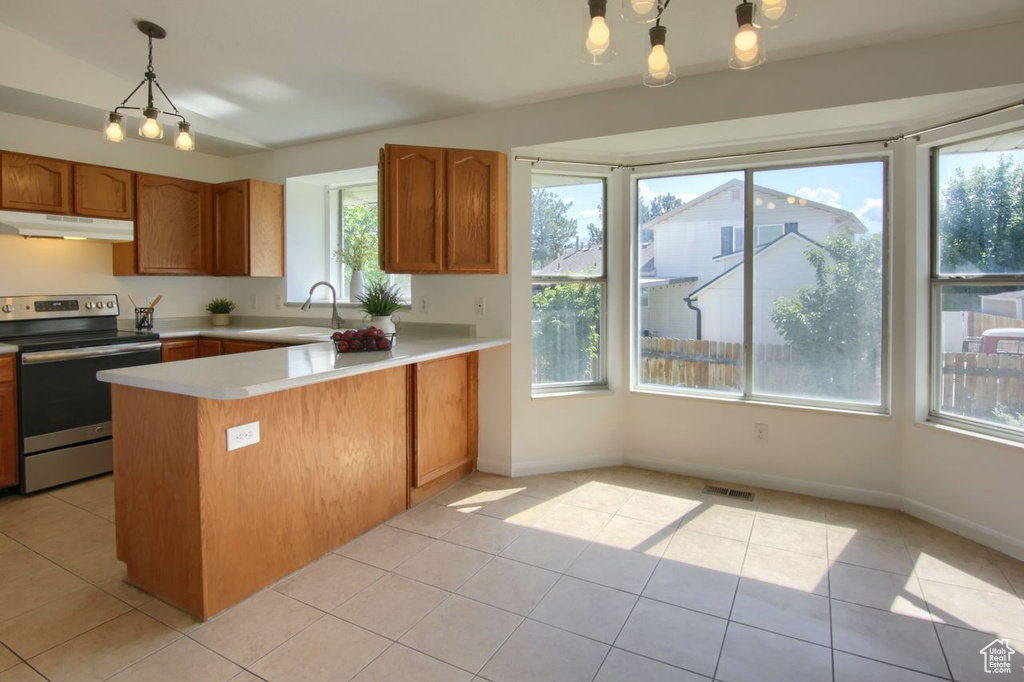 Kitchen with stainless steel electric range oven, under cabinet range hood, a sink, a peninsula, and light countertops