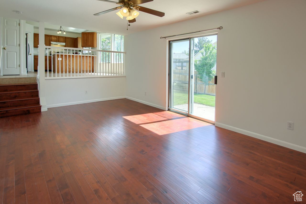 Spare room with a ceiling fan, baseboards, dark wood-style flooring, and stairs