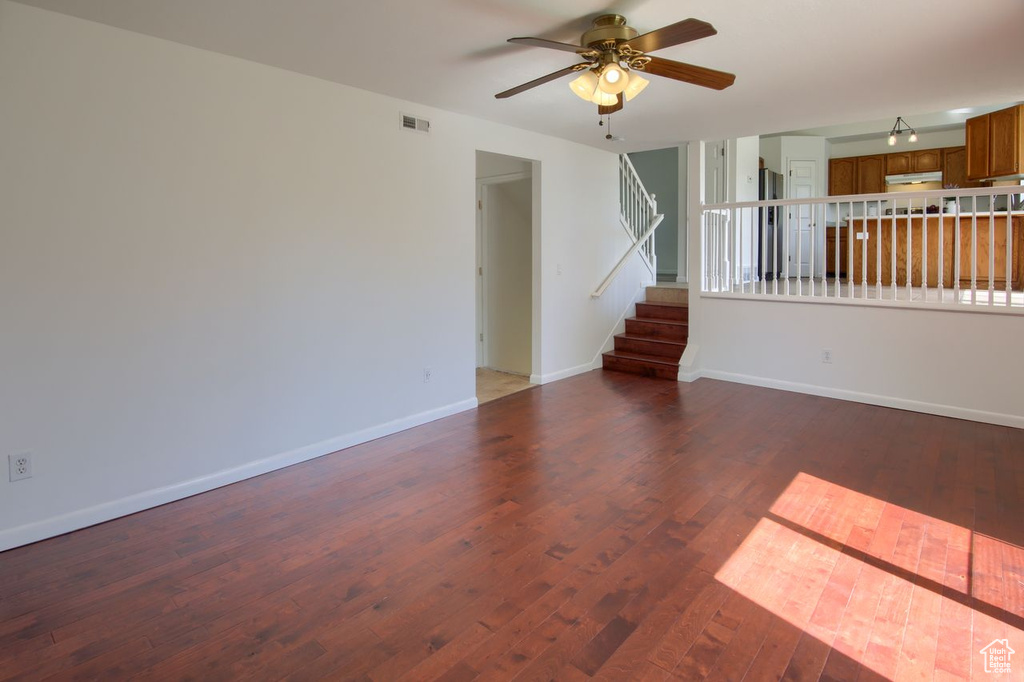 Unfurnished living room featuring ceiling fan, wood finished floors, baseboards, and stairway
