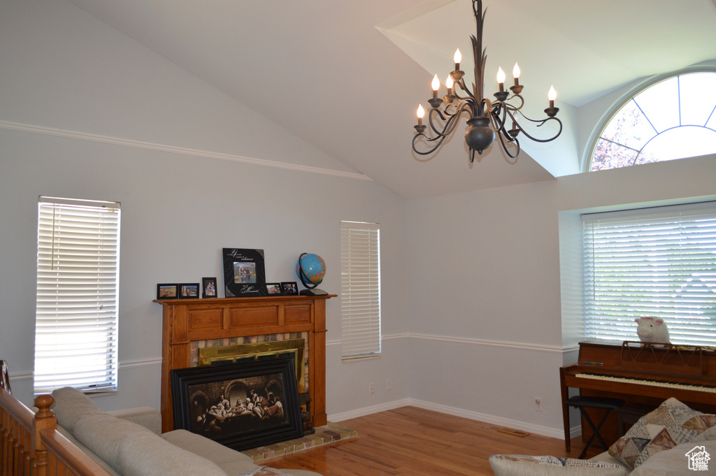 Living area featuring wood finished floors, a fireplace with raised hearth, a chandelier, baseboards, and high vaulted ceiling