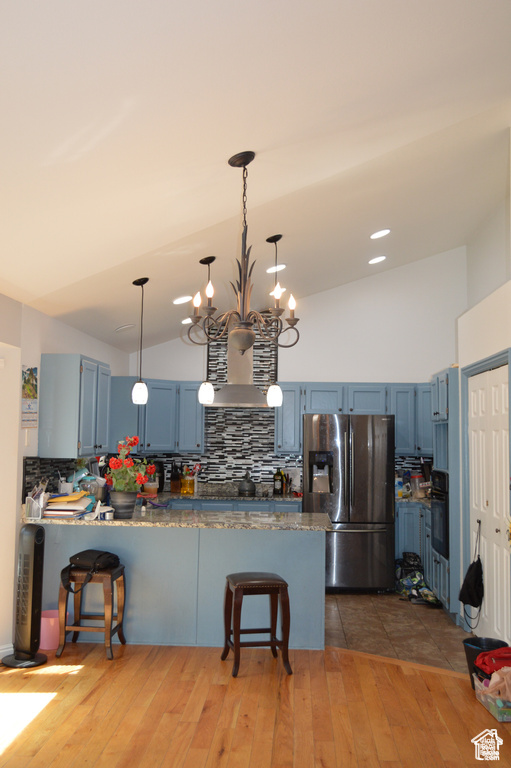 Kitchen with stainless steel refrigerator with ice dispenser, oven, blue cabinets, a peninsula, and backsplash
