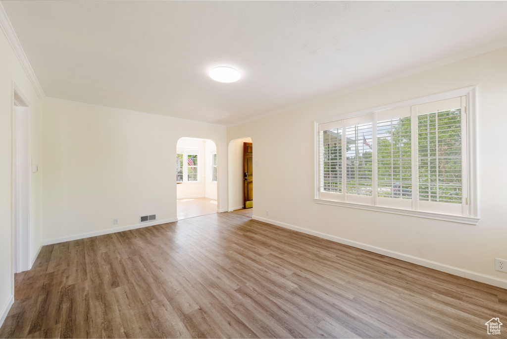 Spare room featuring arched walkways, wood finished floors, plenty of natural light, crown molding, and baseboards