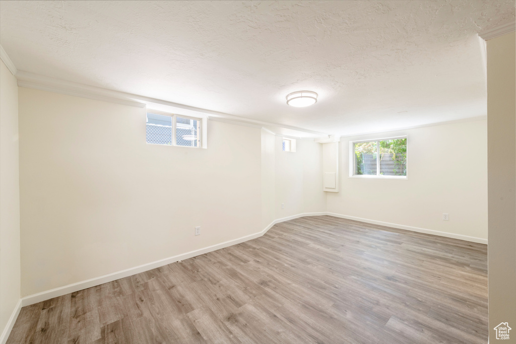 Basement featuring wood finished floors, baseboards, a textured ceiling, and crown molding