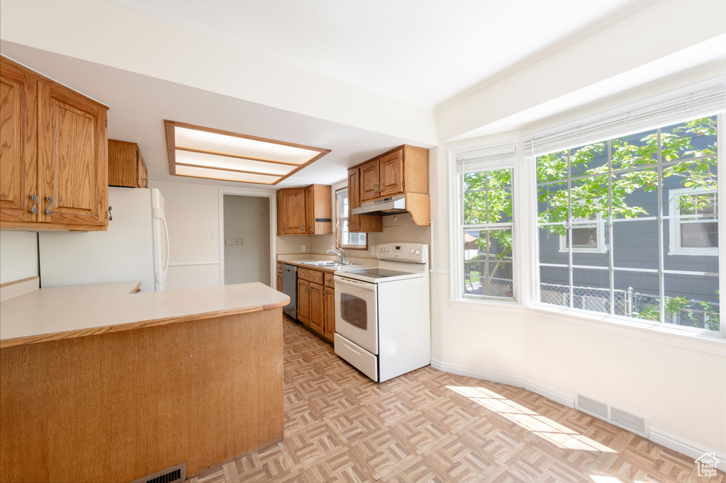 Kitchen featuring white appliances, a sink, light countertops, and healthy amount of natural light